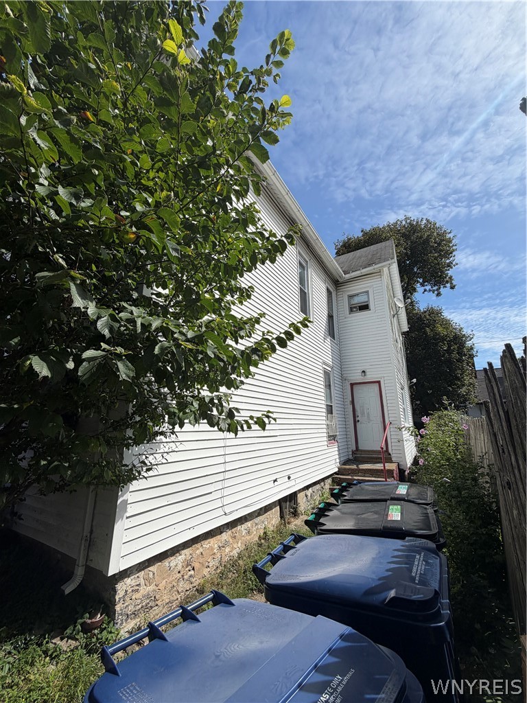 Side exterior of a white-sided house with a red-trimmed entrance beside a fenced walkway.