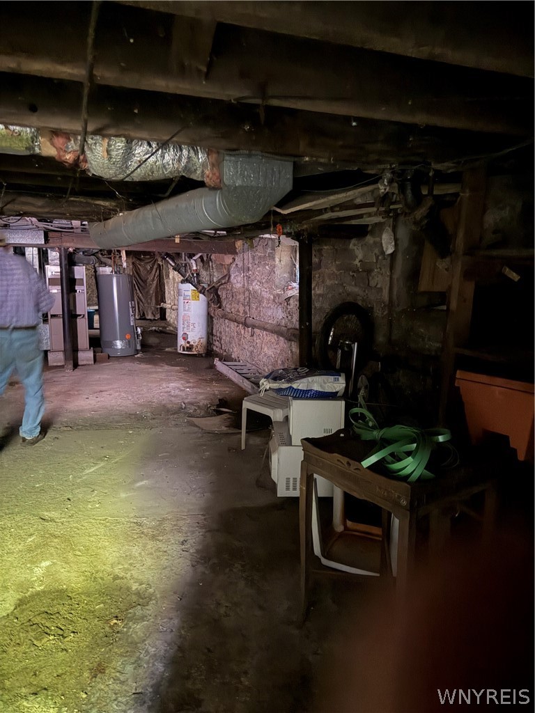 Unfinished basement with exposed beams, overhead ductwork, heating equipment, and stored items.