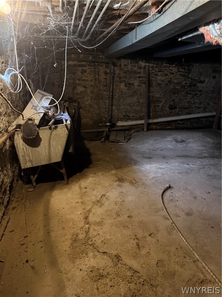 Unfinished basement with stone walls, exposed pipes, and utility equipment.