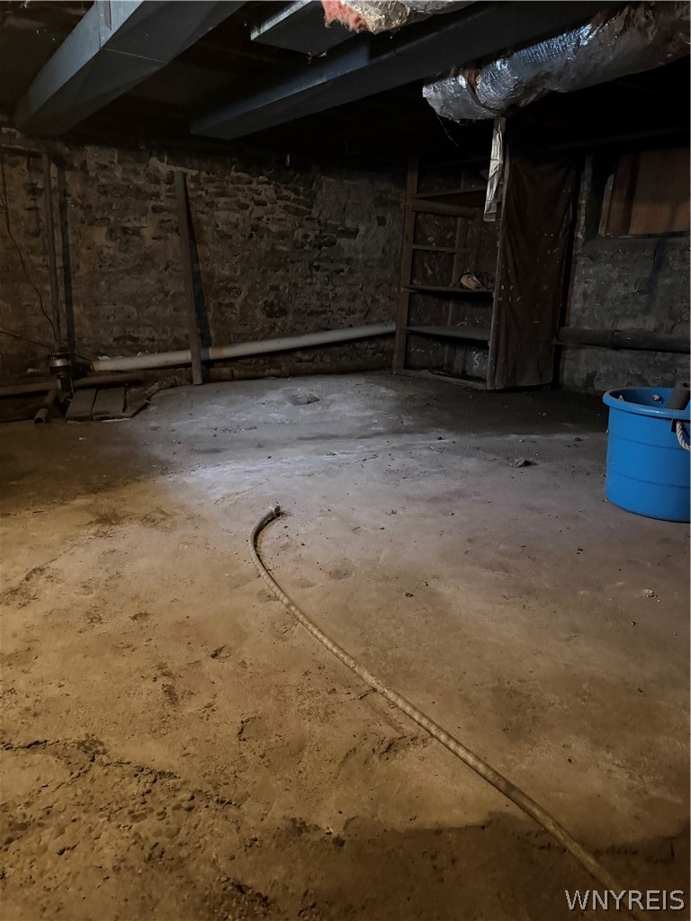 Unfinished basement with exposed stone walls, ceiling joists, and a concrete floor.
