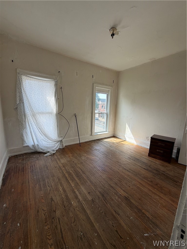 Mostly empty room with worn hardwood floors, two windows, and a small dresser.