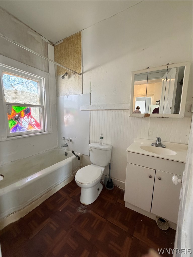 Bathroom with a colorful stained-glass window, bathtub, toilet, and white vanity.