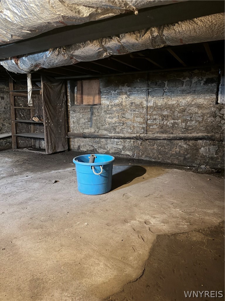 Unfinished basement with exposed stone walls, low insulated ceiling, and concrete floor.