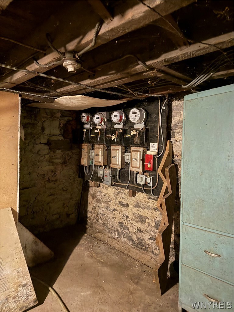 Basement utility area with multiple electric meters and panels on a stone foundation wall.