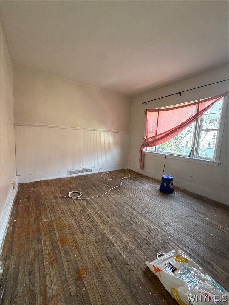 Empty room with worn hardwood floors, paneled walls, and a wide window with a draped pink curtain.