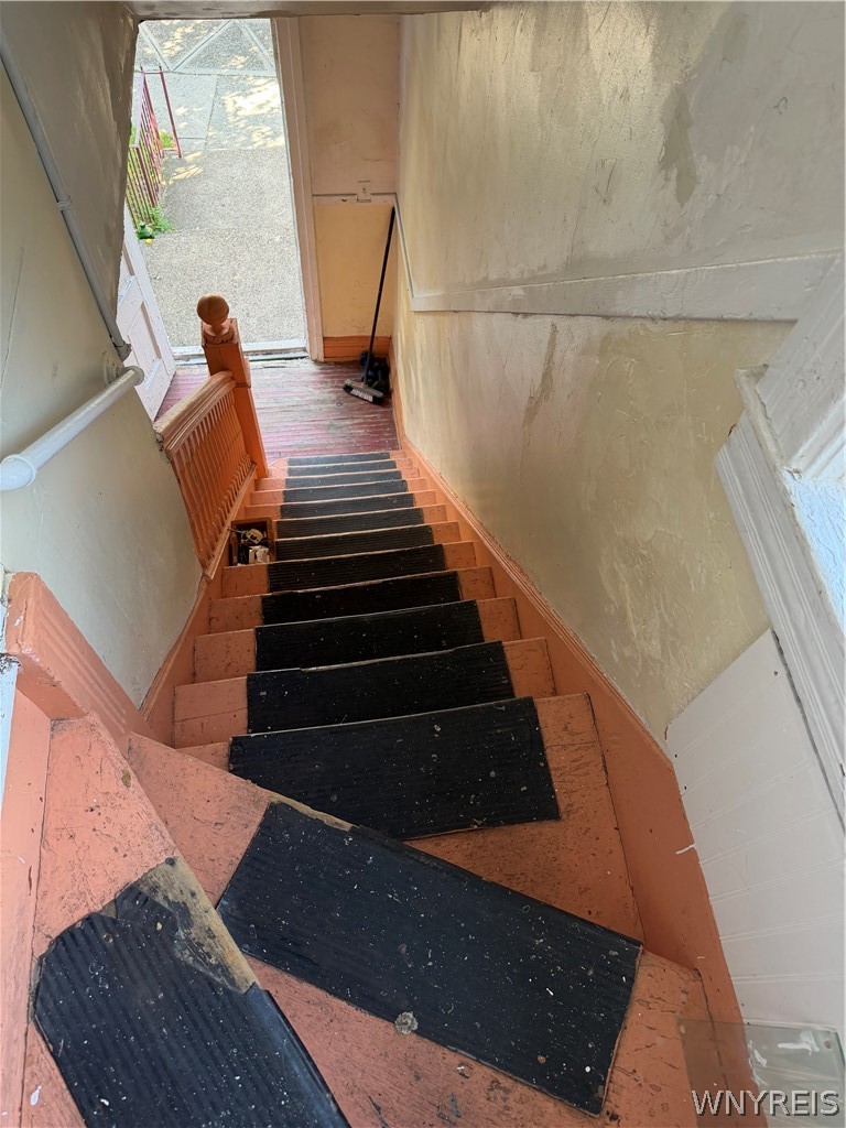 Worn staircase with black tread coverings leads down to an open exterior door.