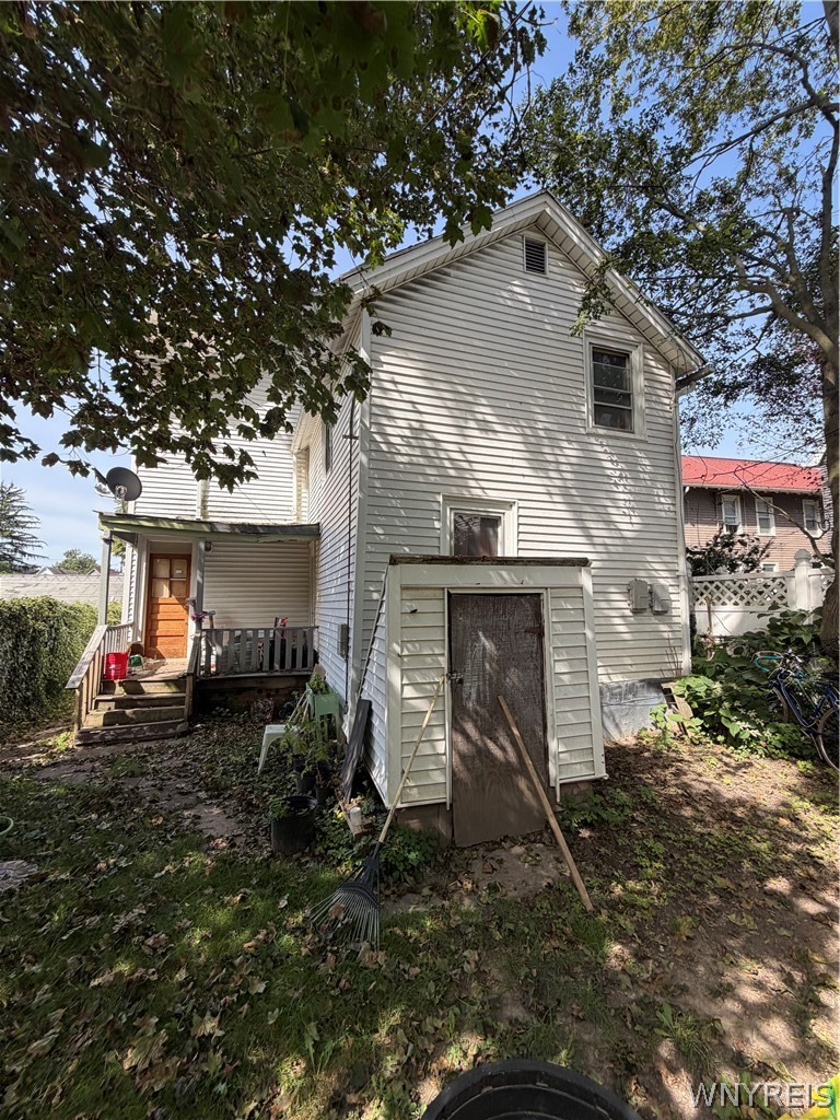 Rear of a two-story light-sided house, shaded by trees, with a small porch and steps.