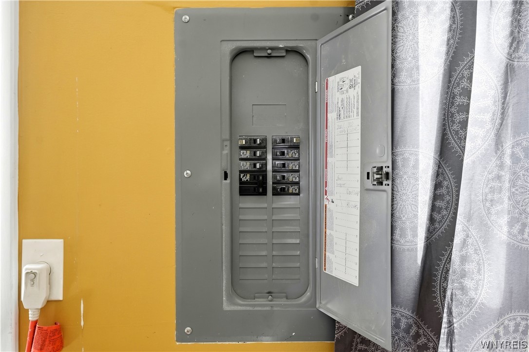 Open electrical breaker panel on a mustard-yellow wall beside a patterned curtain.
