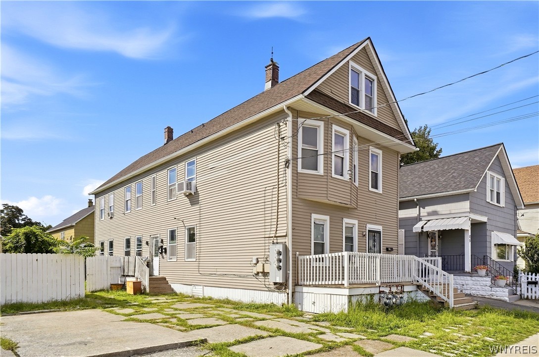 Beige two-story house with a steep front gable, white porch railing, and concrete driveway.