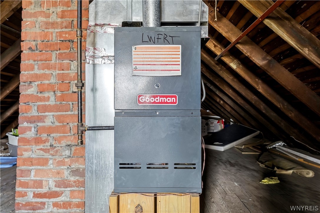 Goodman furnace in an unfinished attic beside an exposed brick chimney.
