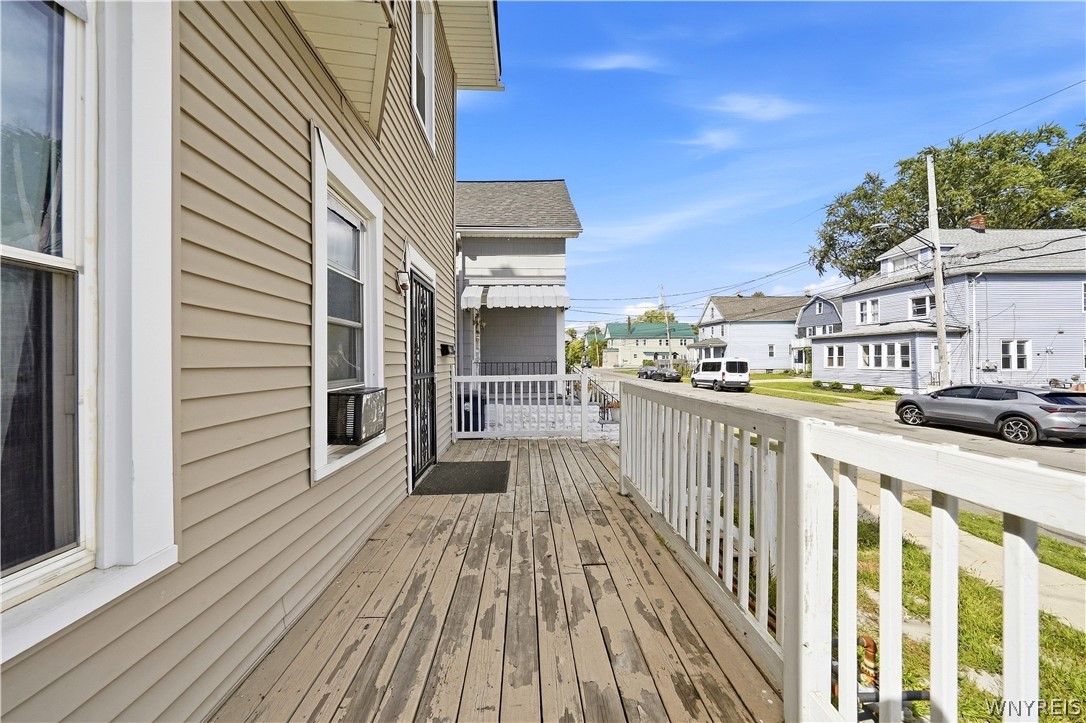 Wooden front porch with white railings beside a beige-sided house, overlooking a residential street.