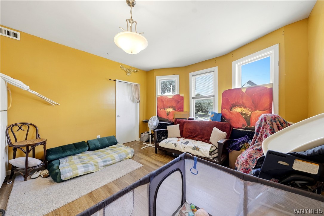 Bedroom with mustard-yellow walls, wood flooring, a futon, sofa, and crib.