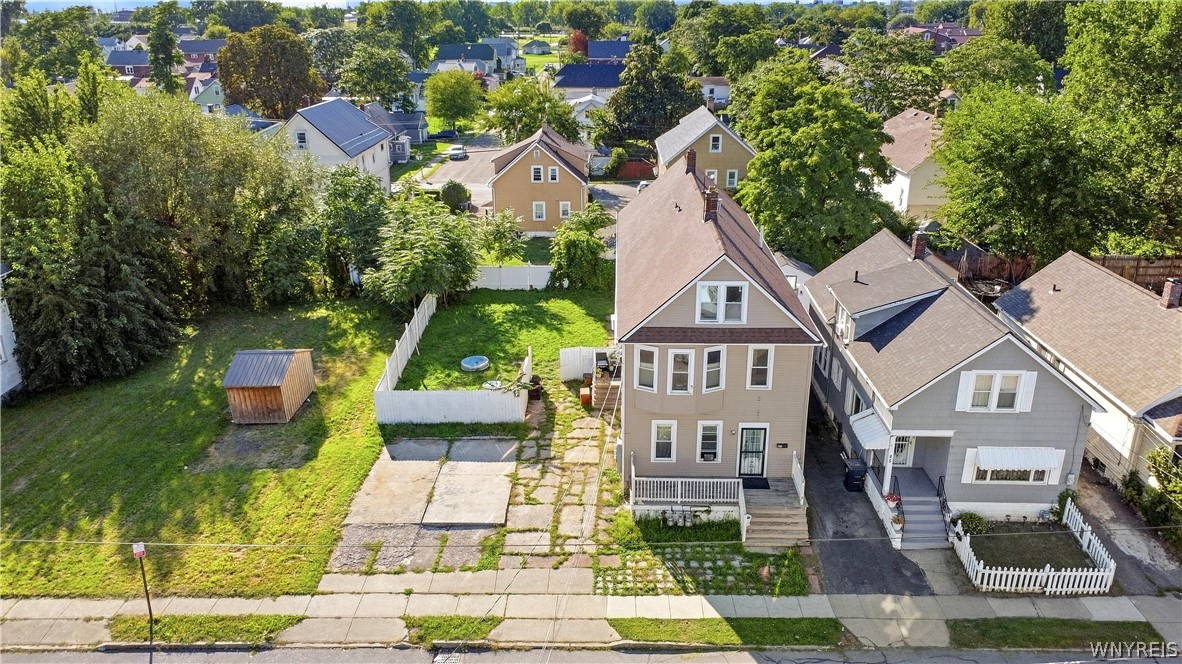 Aerial view of a tan two-story house with a steep gable, porch, and large grassy yard.
