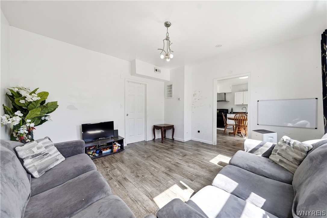 Living room with gray sectional sofas, wood-look floors, and an open doorway to the kitchen.
