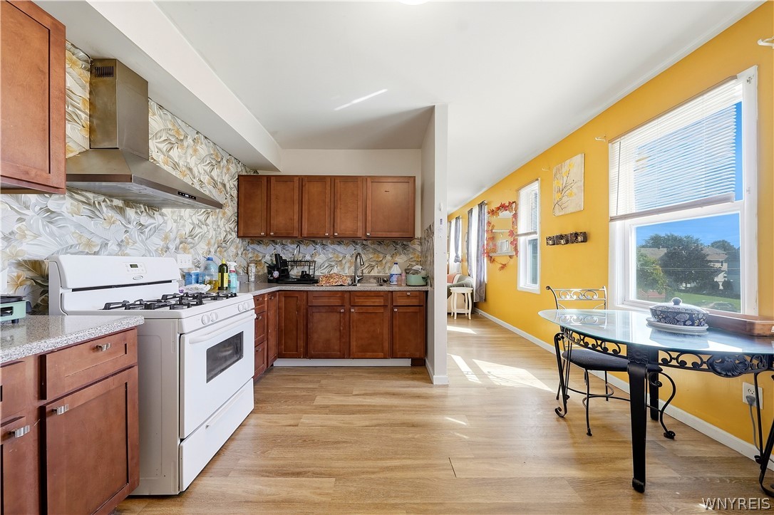 Kitchen with wood cabinets and white gas range opening to a sunny dining area with a glass-top table.