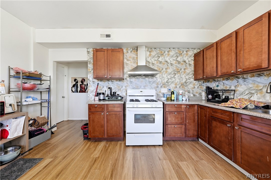 Kitchen with reddish-brown cabinets, a white gas stove, and a patterned floral backsplash.