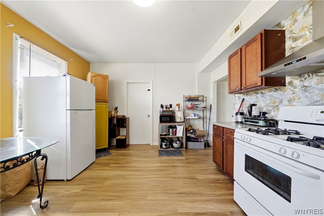 Kitchen with wood cabinets and flooring, white appliances, and a floral backsplash.