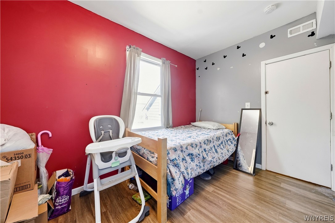 Bedroom with a red accent wall, patterned bedspread, and high chair.