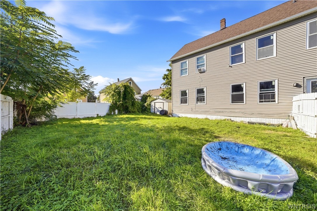 Two-story beige house beside a grassy fenced backyard with a small blue inflatable pool.