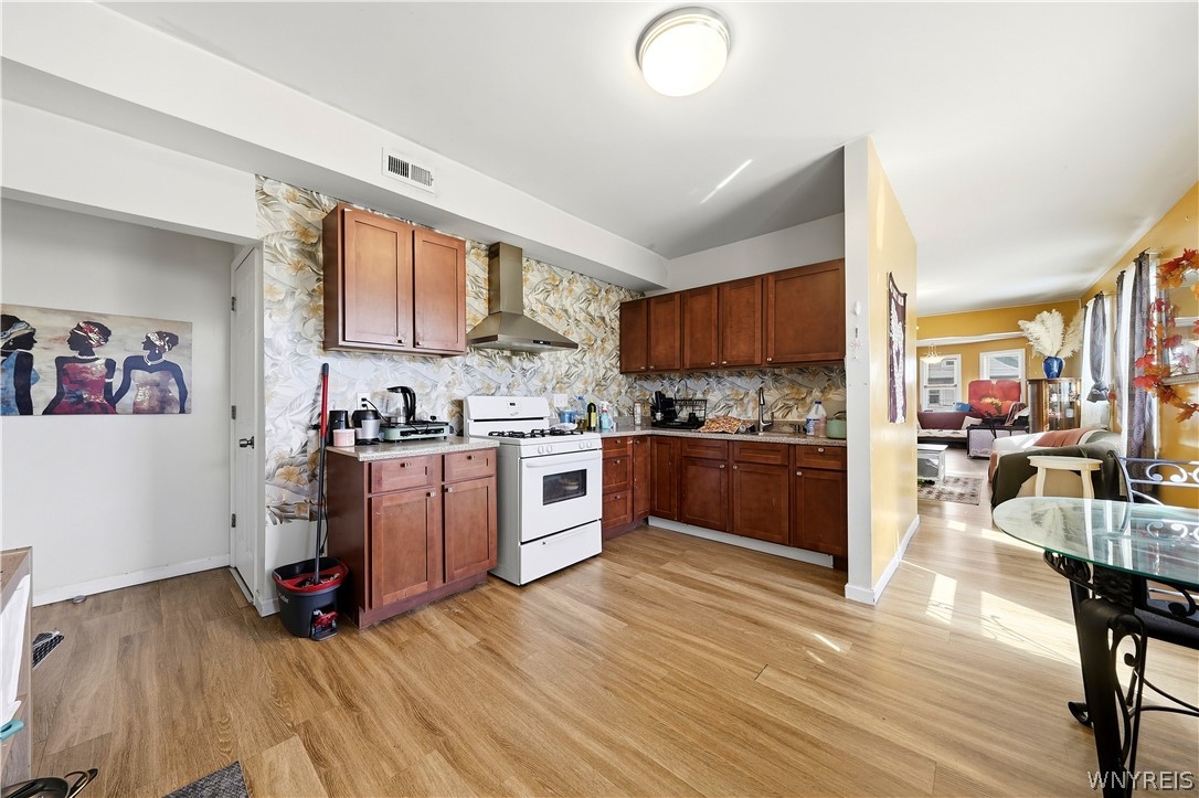 Kitchen with wood cabinets and floral backsplash opening into a furnished living room.