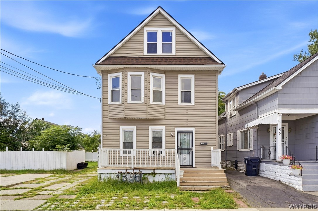 Beige two-story house with a steep gable, white-trimmed windows, and a small front porch.