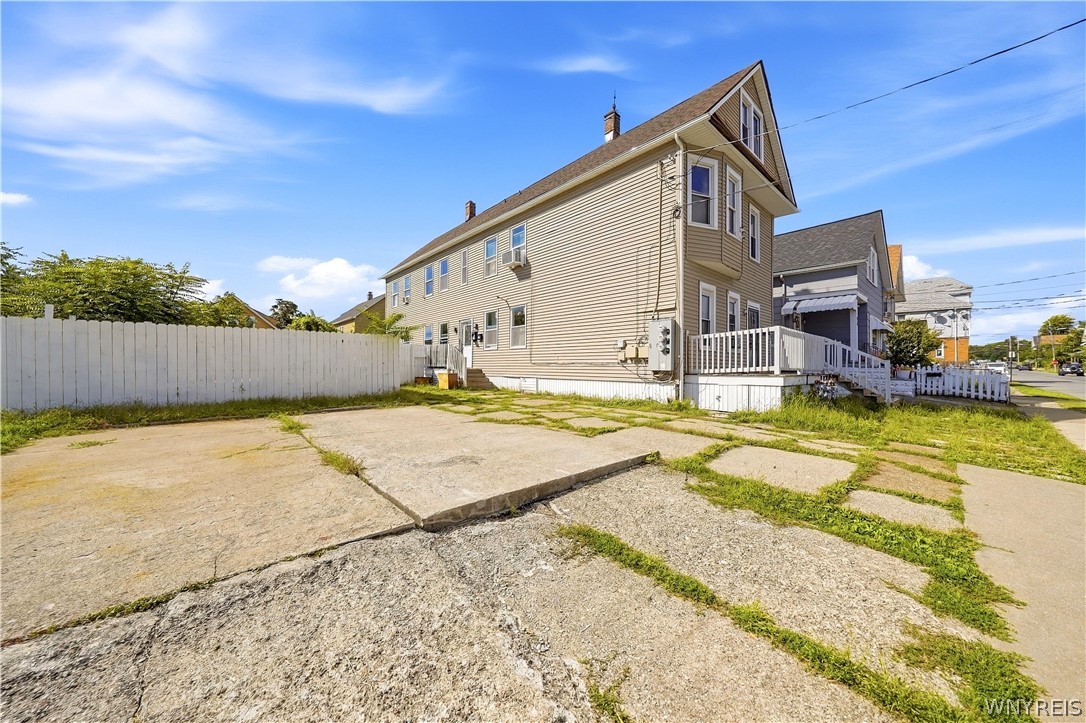 Beige multi-story house with a covered porch, white fence, and wide concrete driveway.