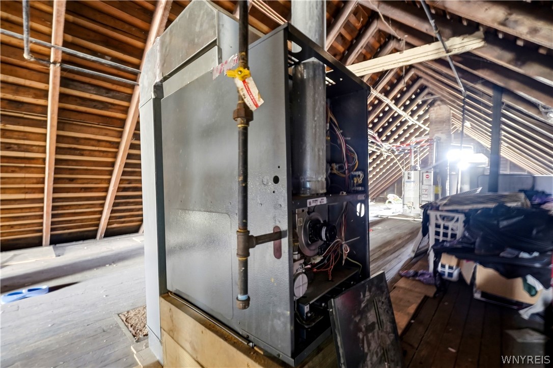 Unfinished attic with exposed rafters, a large furnace, and stored items.
