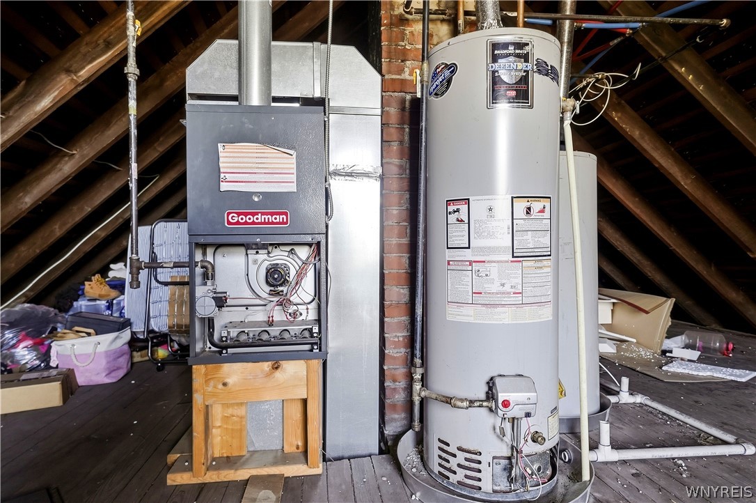Furnace and water heater in an unfinished attic utility area with exposed rafters.