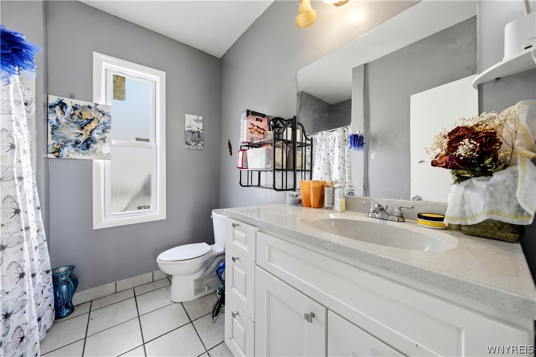 Bathroom with a white vanity, large mirror, toilet, and window with floral curtains.