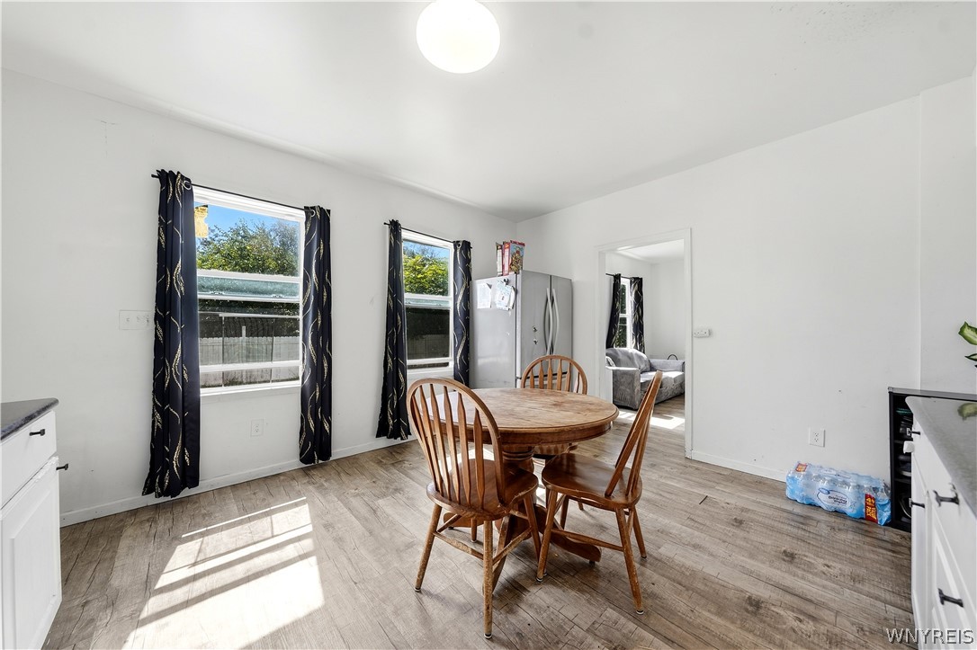 Dining area with a round wooden table, curtained windows, and an open doorway to a bedroom.