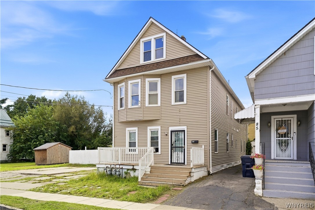 Tan two-story house with a steep gable, white-trimmed windows, and a small front porch.
