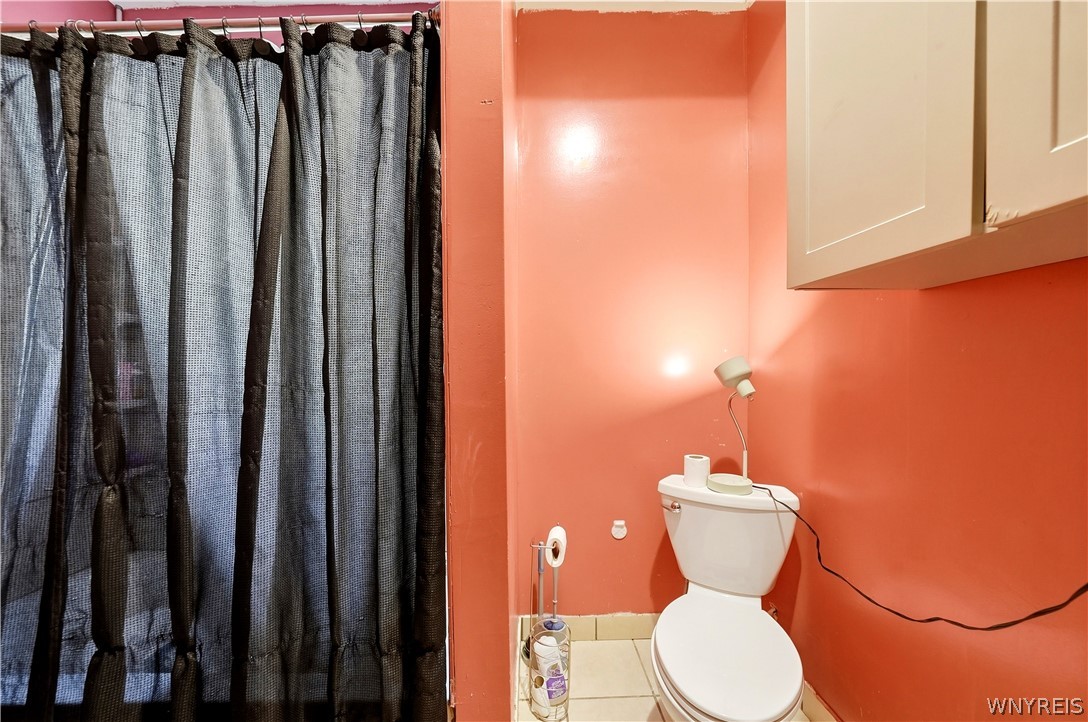 Small bathroom with a white toilet, dark shower curtain, and salmon-colored walls.