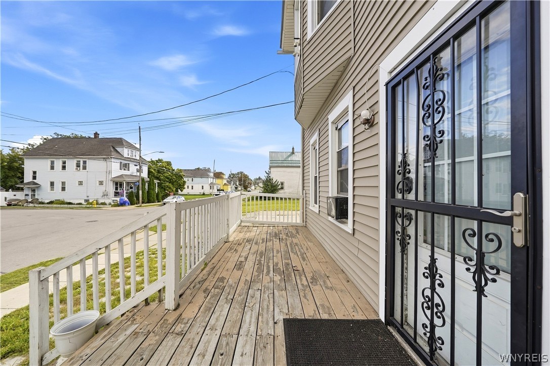 Front porch deck with weathered wood boards, white railings, and a decorative black security door.