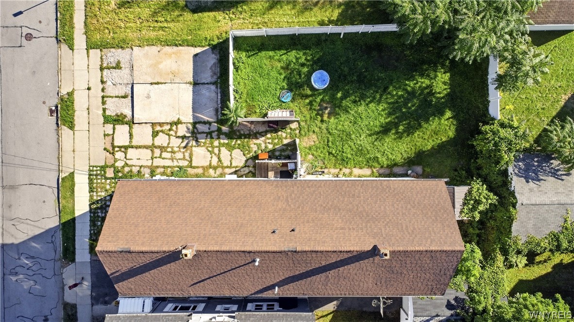 Aerial view of a home with a long brown roof and fenced green backyard.