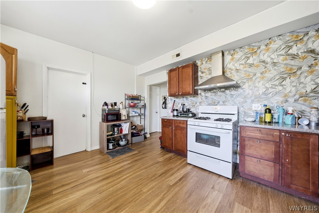 Kitchen with wood cabinets, white range, floral backsplash, and wood-look flooring.