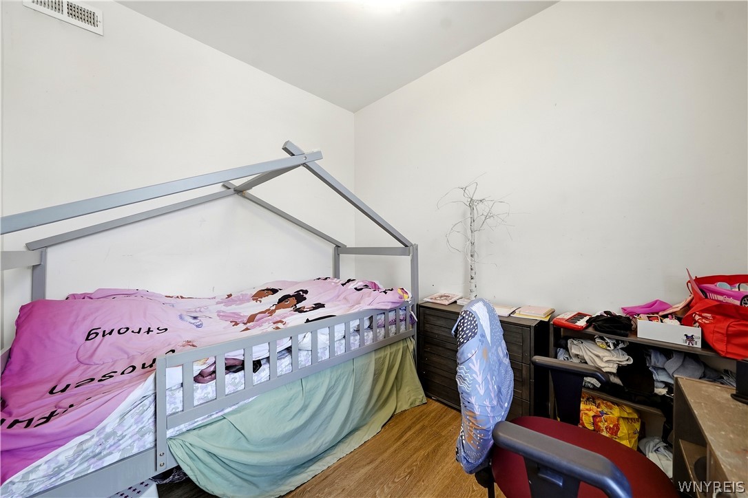 Bedroom with a metal-frame bed, pink cartoon bedding, and a crowded desk area.