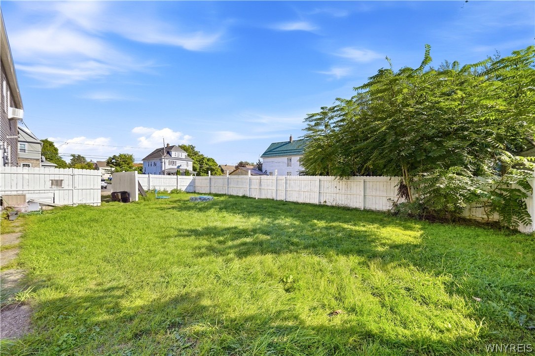 Fenced backyard with a broad grassy lawn and a large leafy tree.