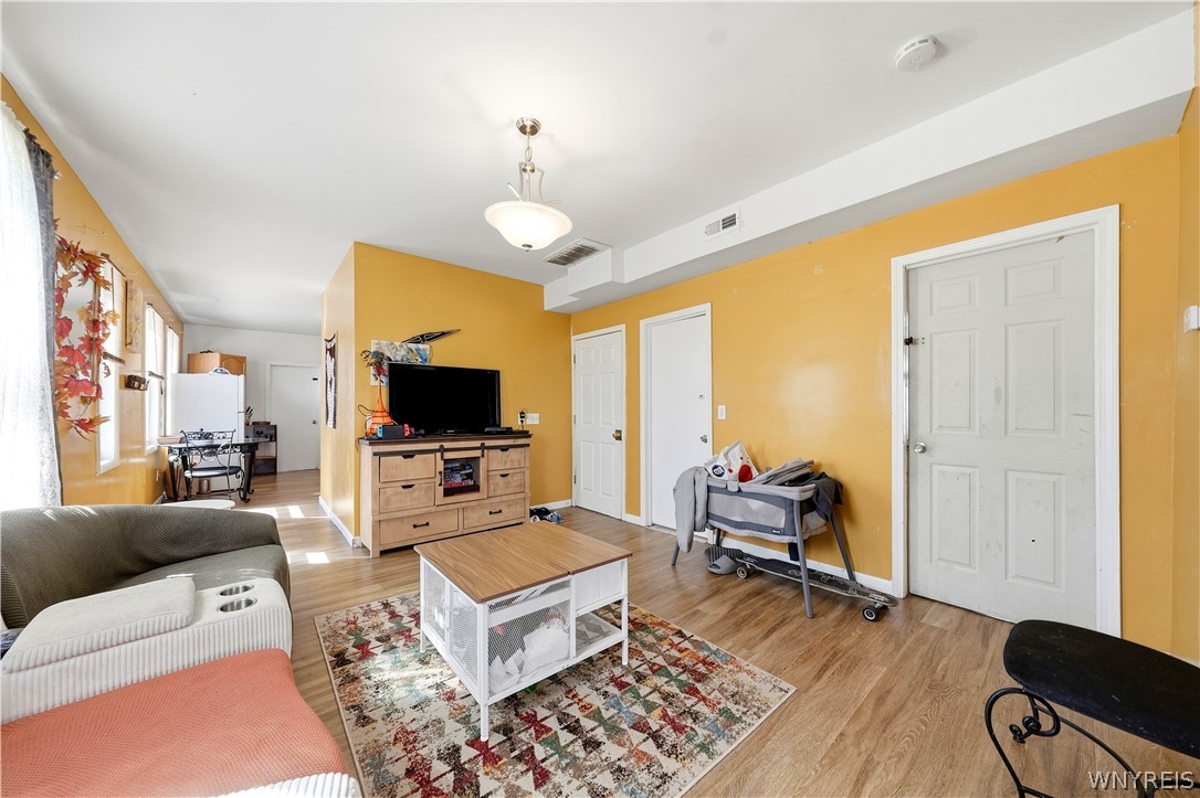 Living room with mustard-yellow walls, patterned rug, sofa, and dining area by the windows.
