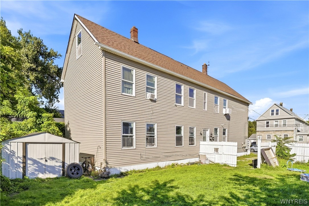 Side of a beige two-story house beside a grassy yard and detached shed.