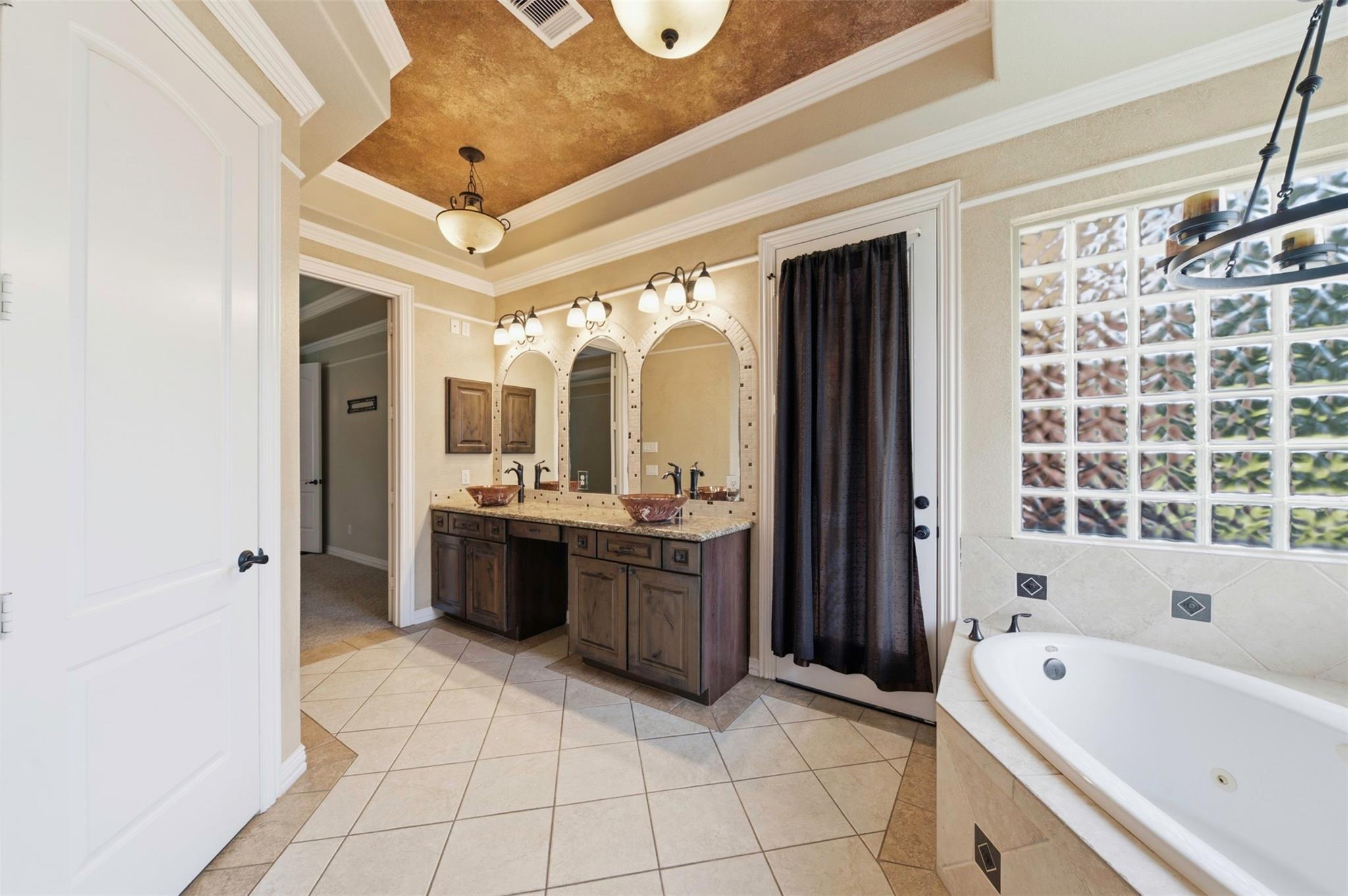 Bathroom with a double vanity, arched mirrors, soaking tub, and glass-block window.