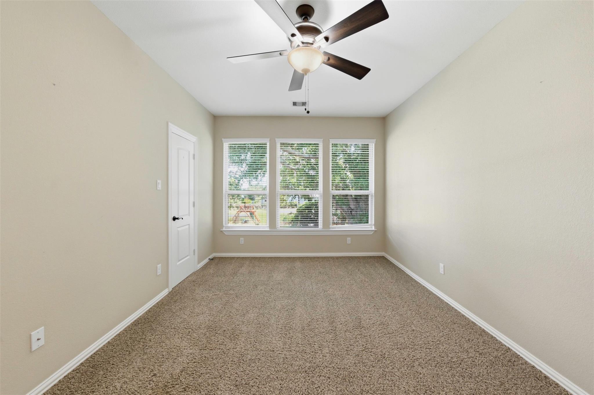 Empty carpeted bedroom with a ceiling fan and three windows with blinds.