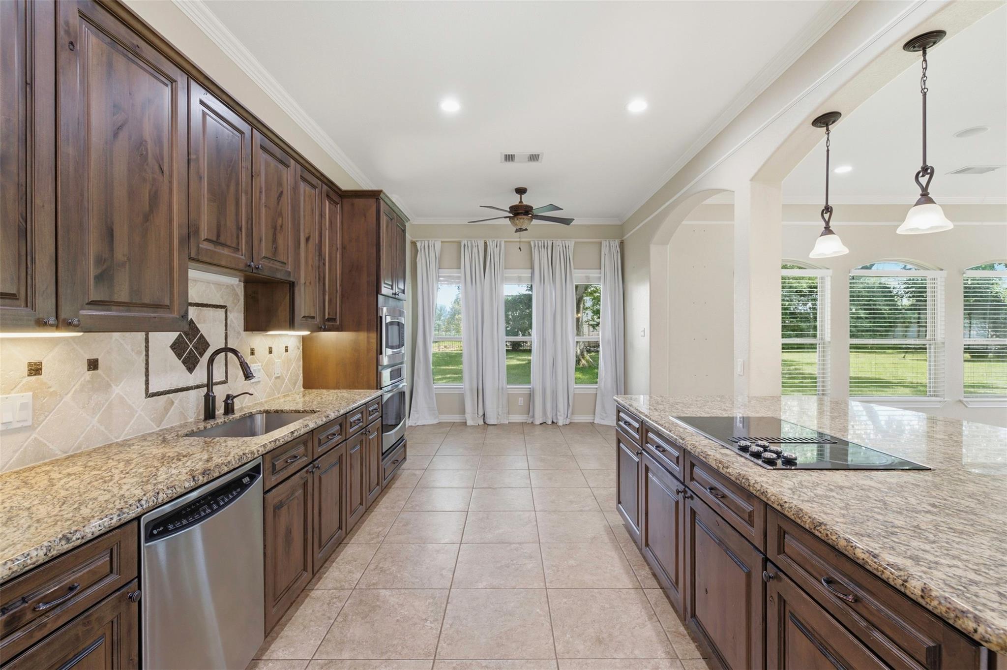 Spacious kitchen with dark wood cabinetry, granite counters, a cooktop island, and windows overlooking the lawn.