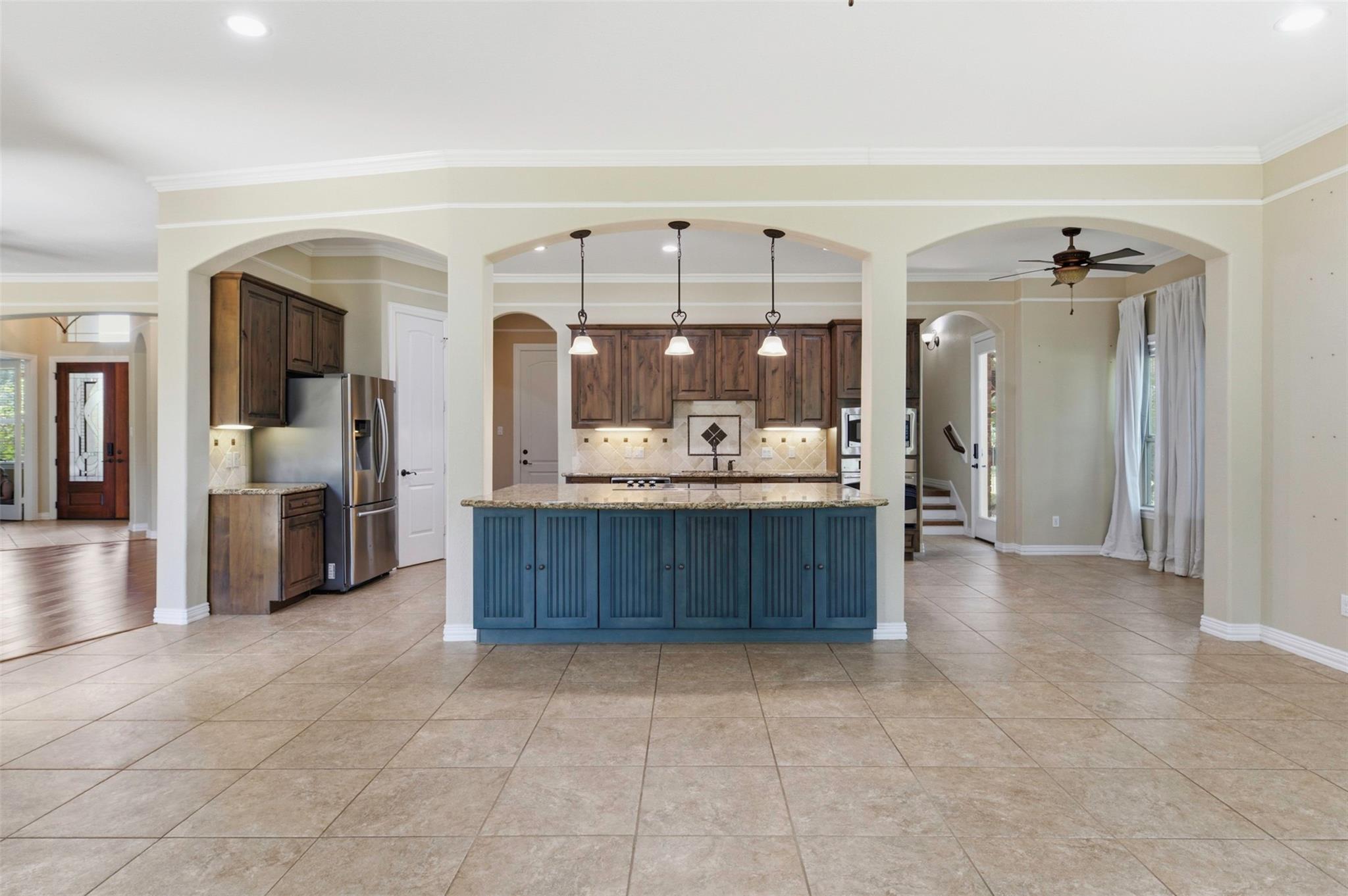 Open kitchen with a blue island, dark wood cabinets, stainless steel appliances, and three pendant lights.