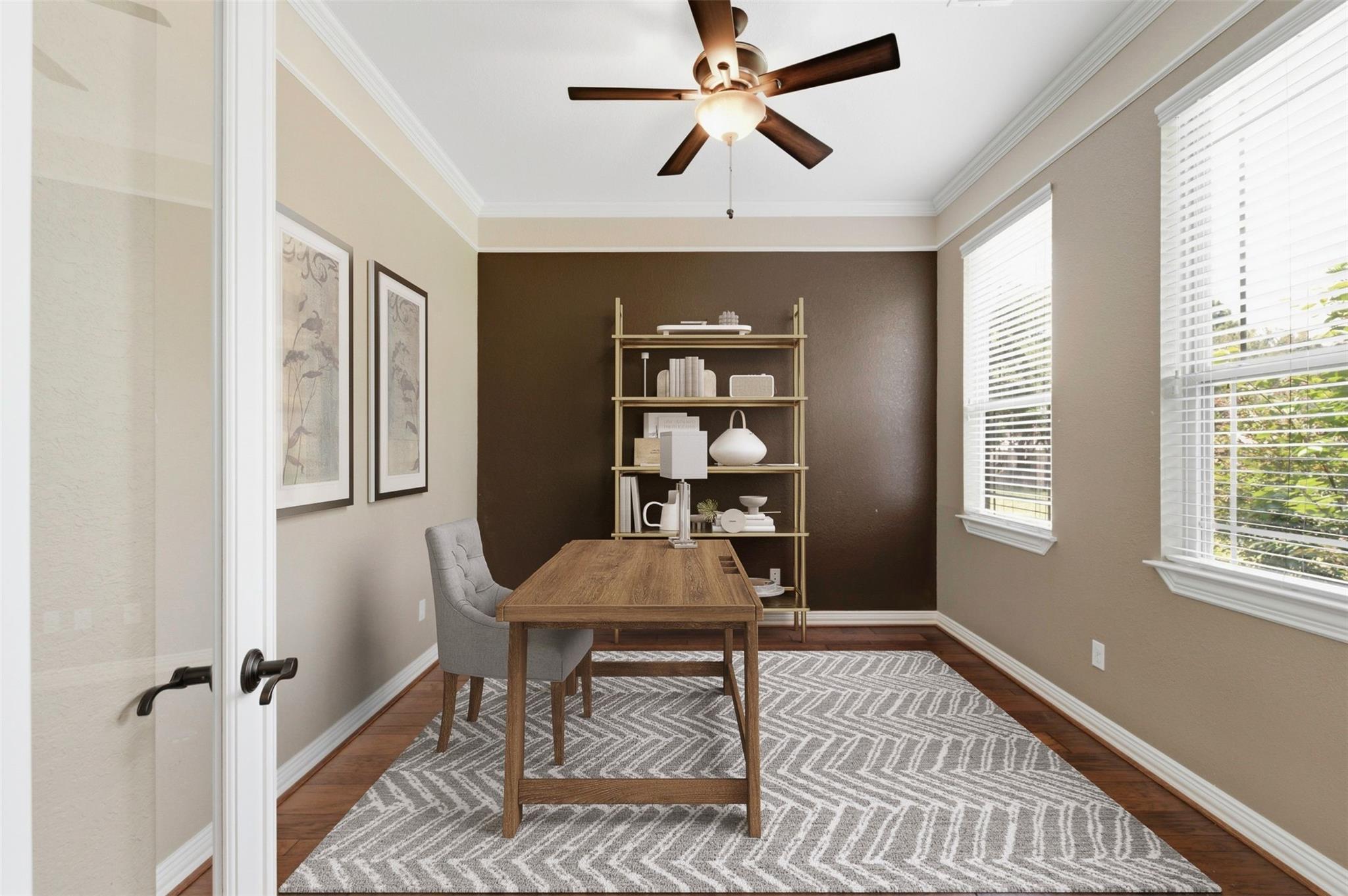 Staged home office with a wooden desk, open shelving against a dark accent wall, and two bright windows.