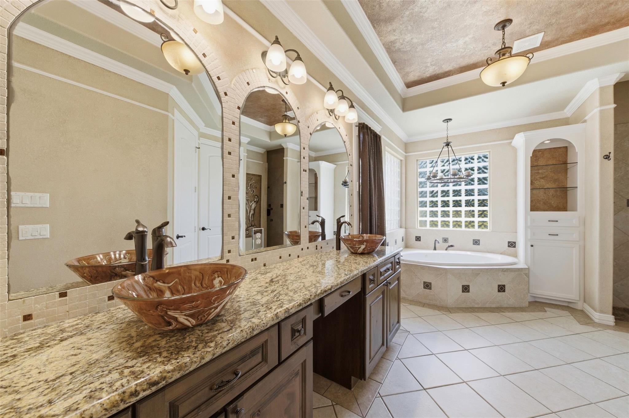 Bathroom with a granite double vanity, decorative vessel sinks, arched mirrors, and a soaking tub beneath a large window.