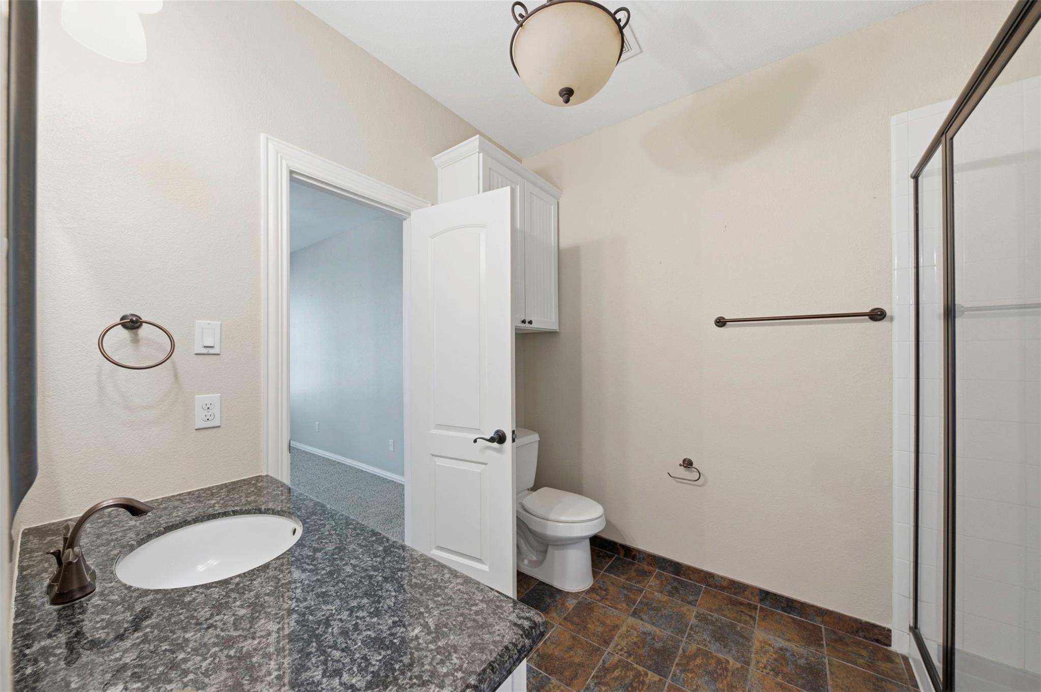 Bathroom with a granite vanity, toilet, and glass-enclosed shower.