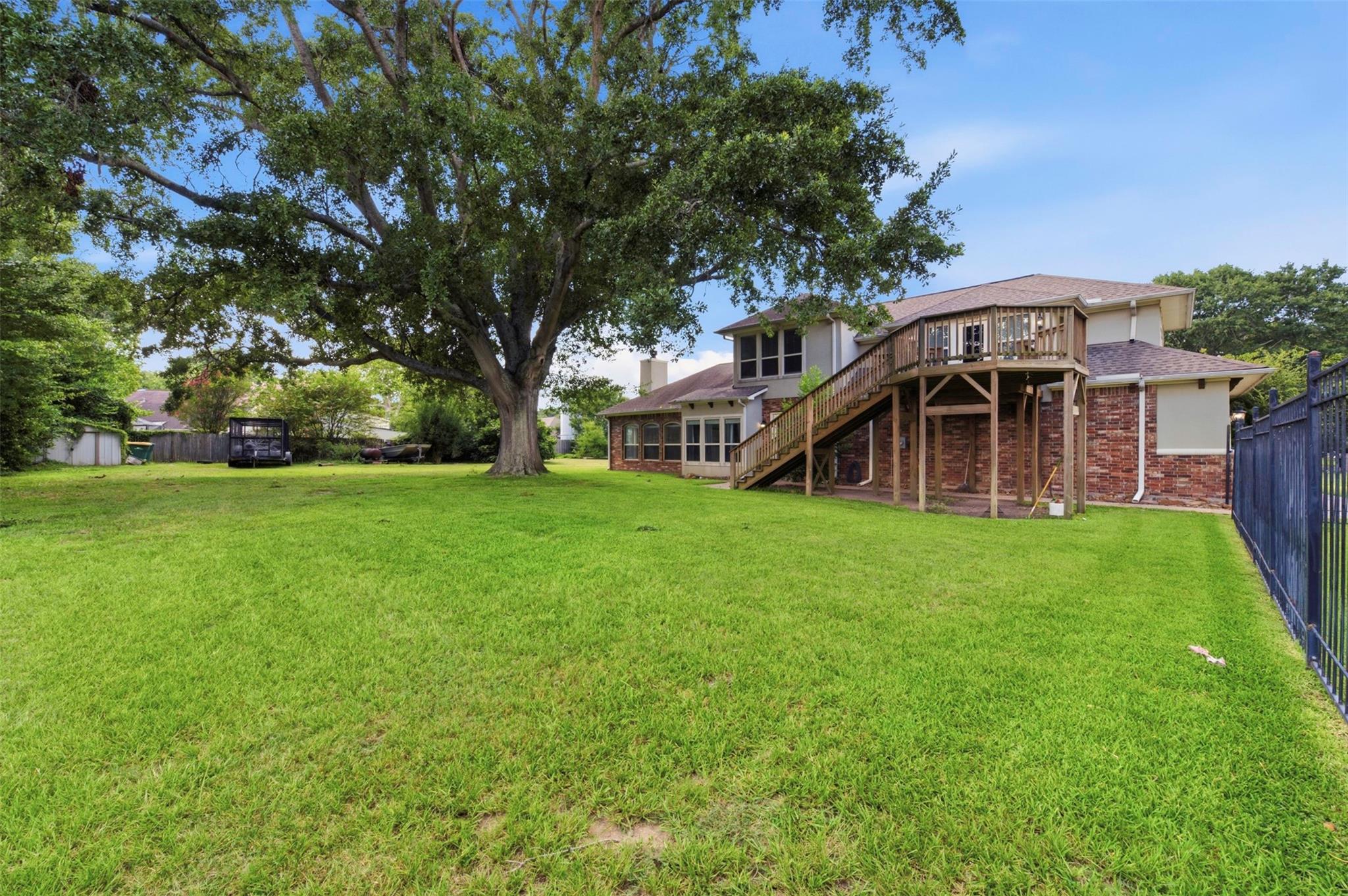 Rear of a two-story home with a raised wooden deck, broad lawn, and mature shade tree.