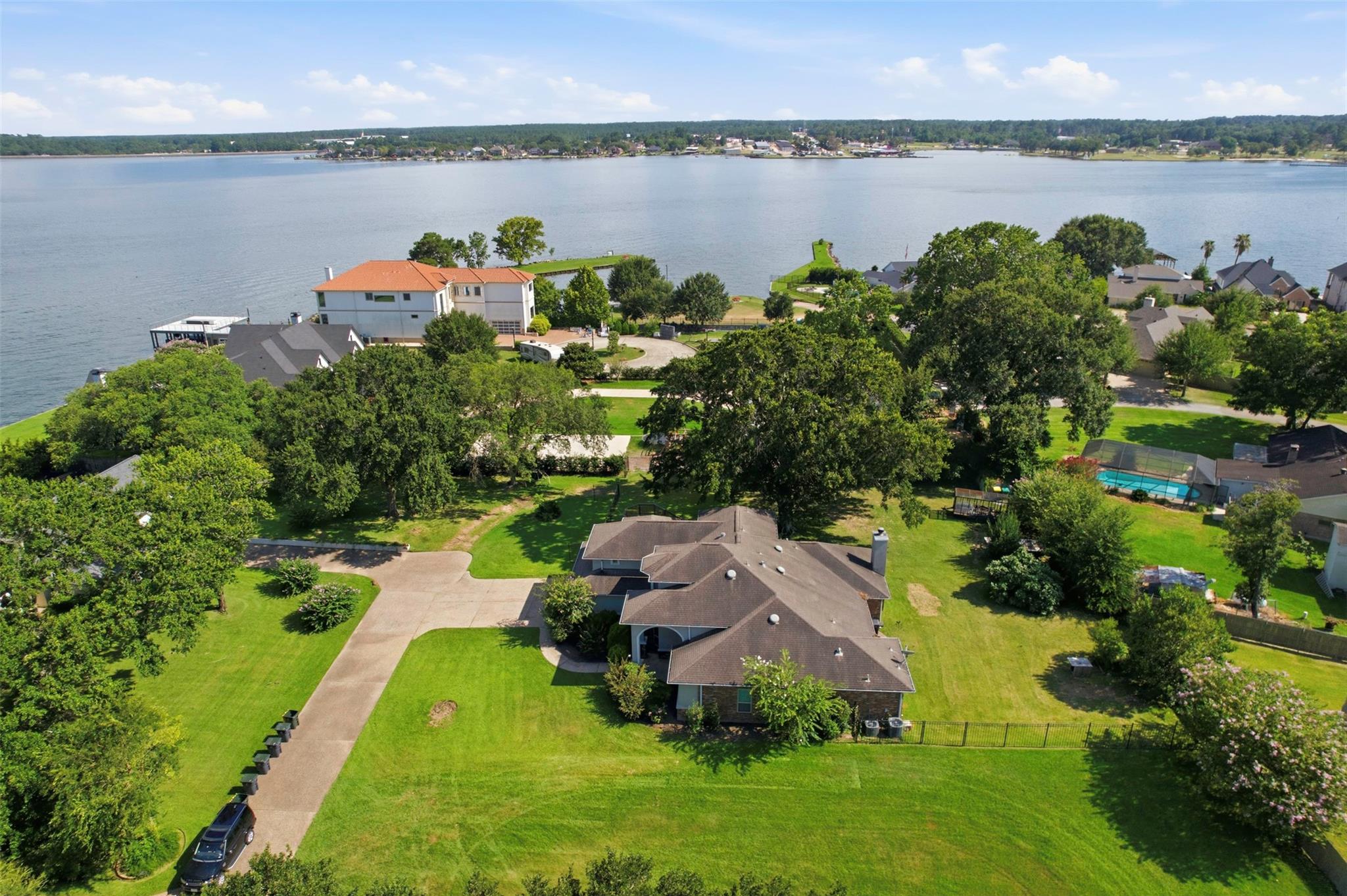 Aerial view of a home beside a lake, with a broad lawn, mature trees, and neighboring waterfront houses.