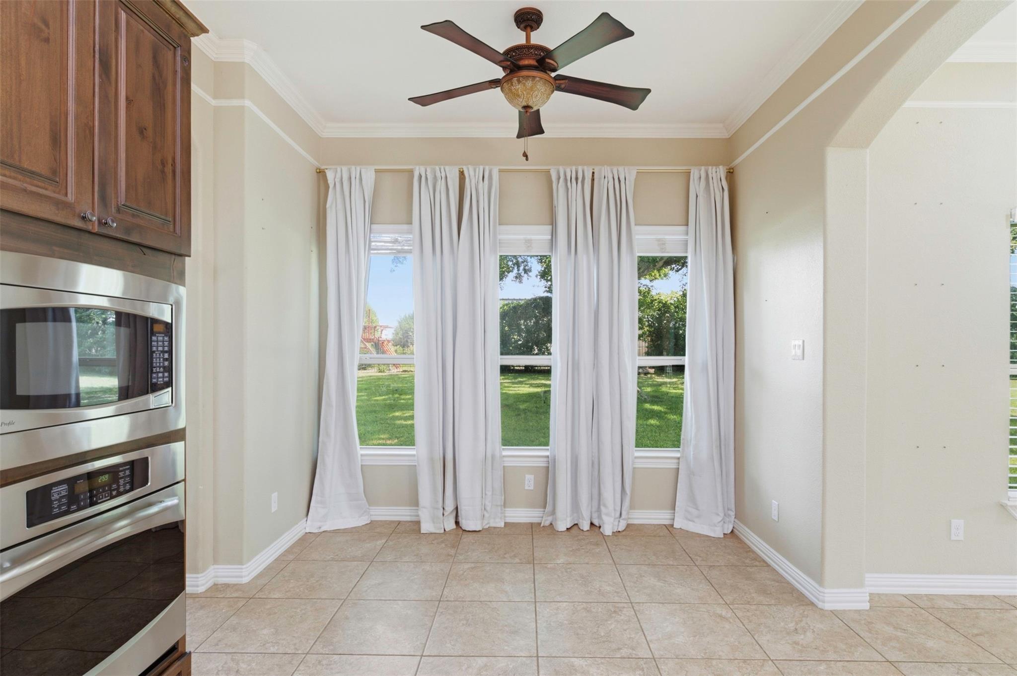 Kitchen with built-in stainless steel appliances, dark wood cabinets, and curtained windows overlooking a lawn.
