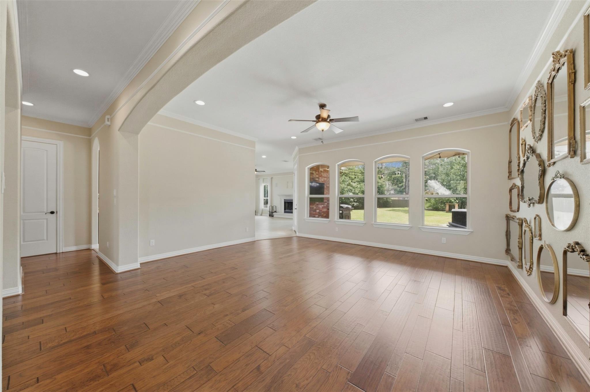 Vacant living room with wood floors, arched windows, and ornate mirrors on the wall.